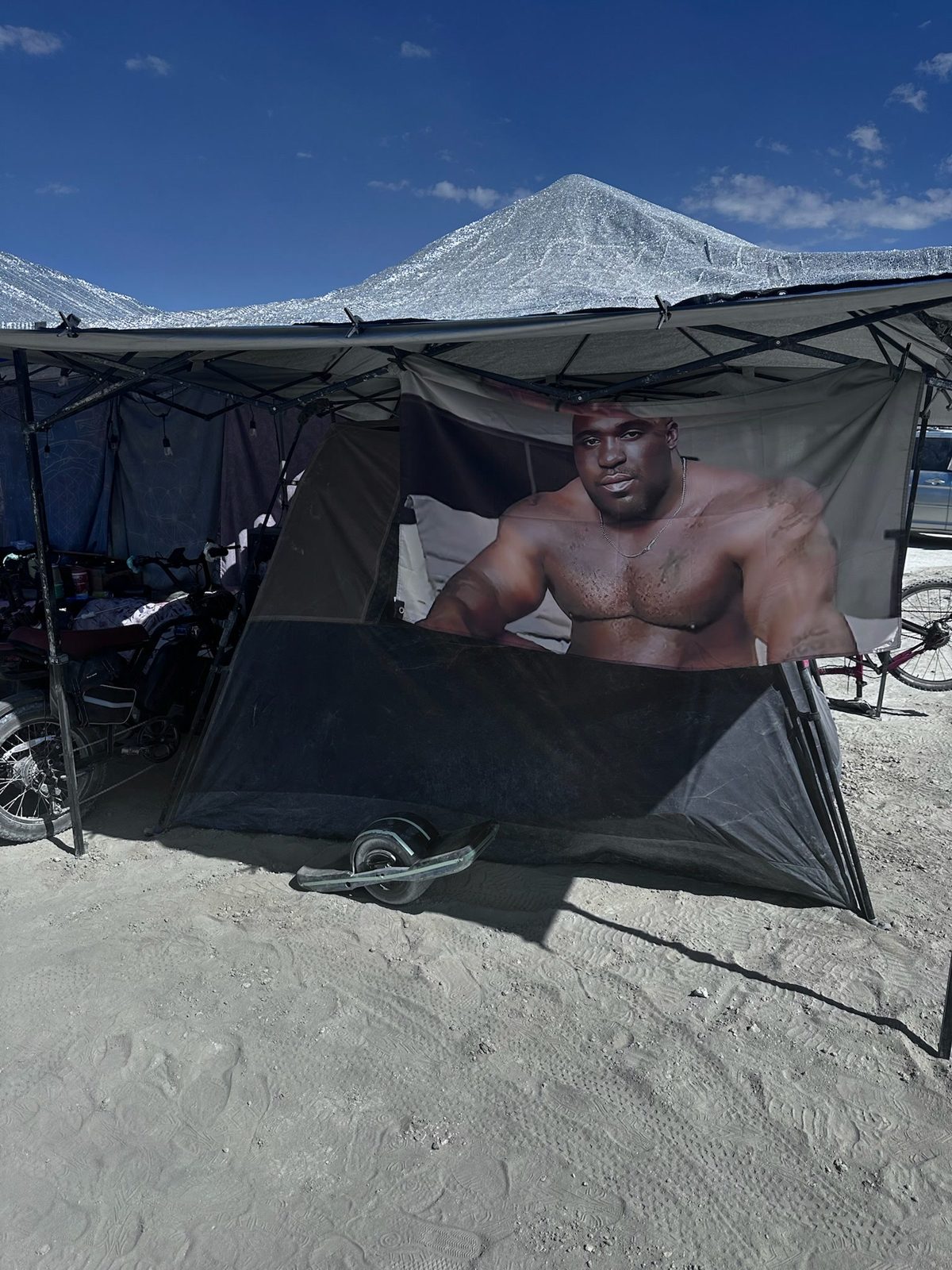 Camper resting inside a dark shade tent at a desert festival