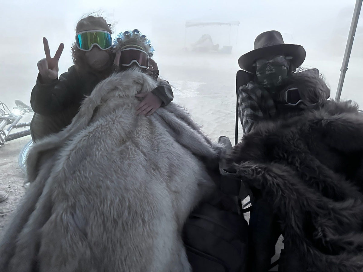 Friends bundled in fur coats and goggles at a dusty festival