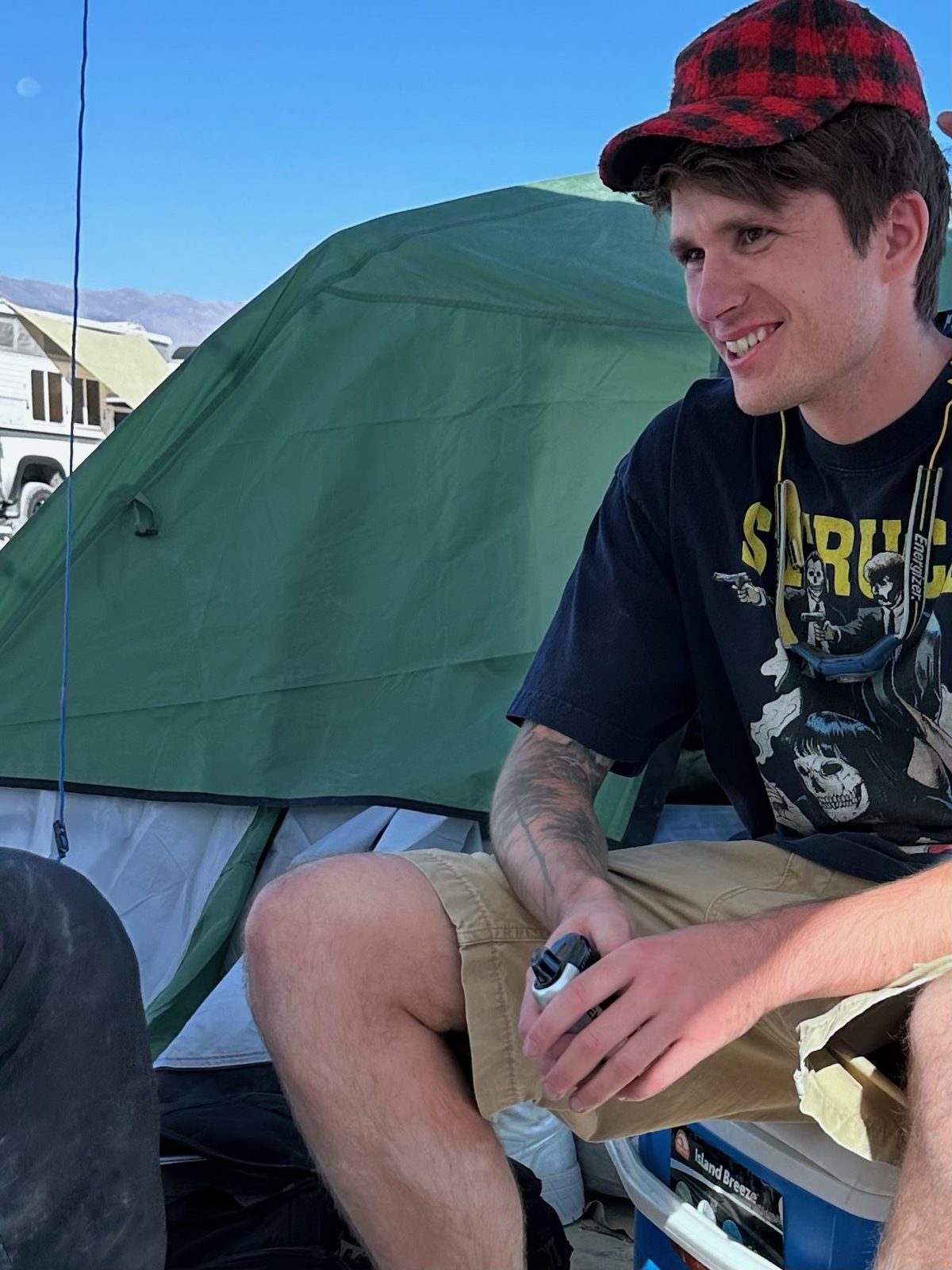 Camper sitting outside a green dome tent at a dusty desert festival camp