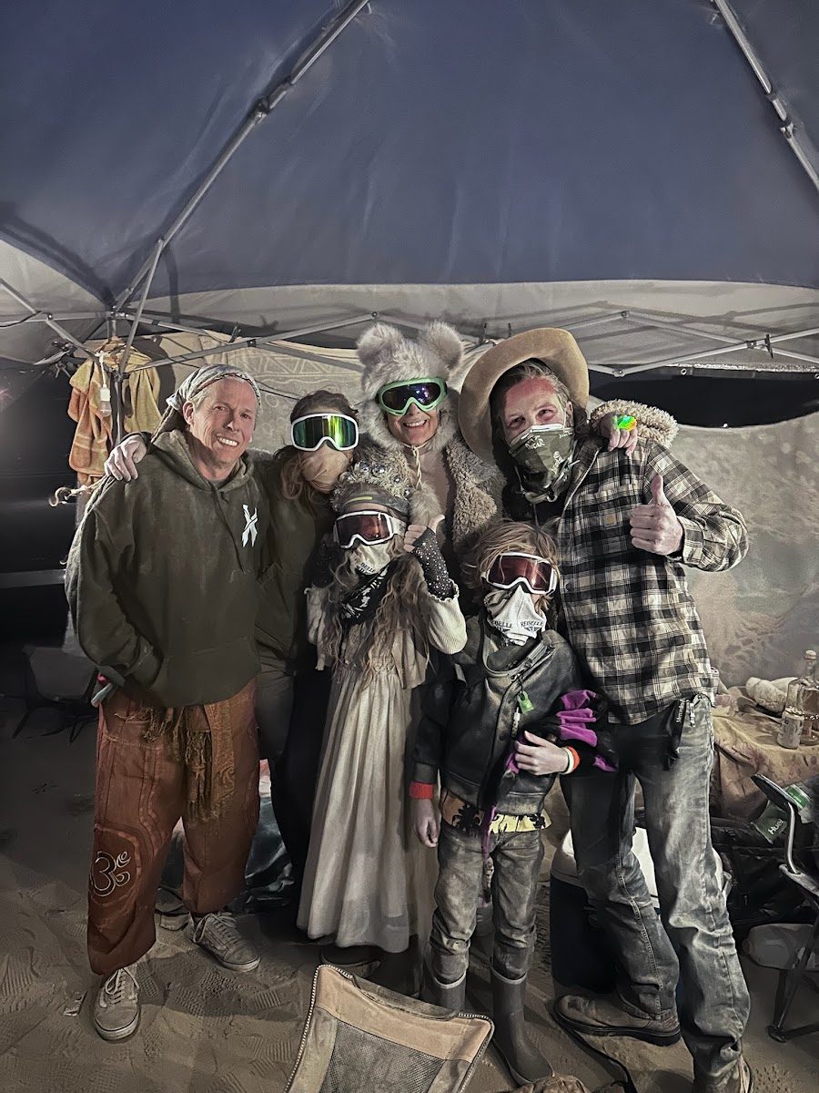 Friends in dust goggles under a shade tent at a desert festival camp