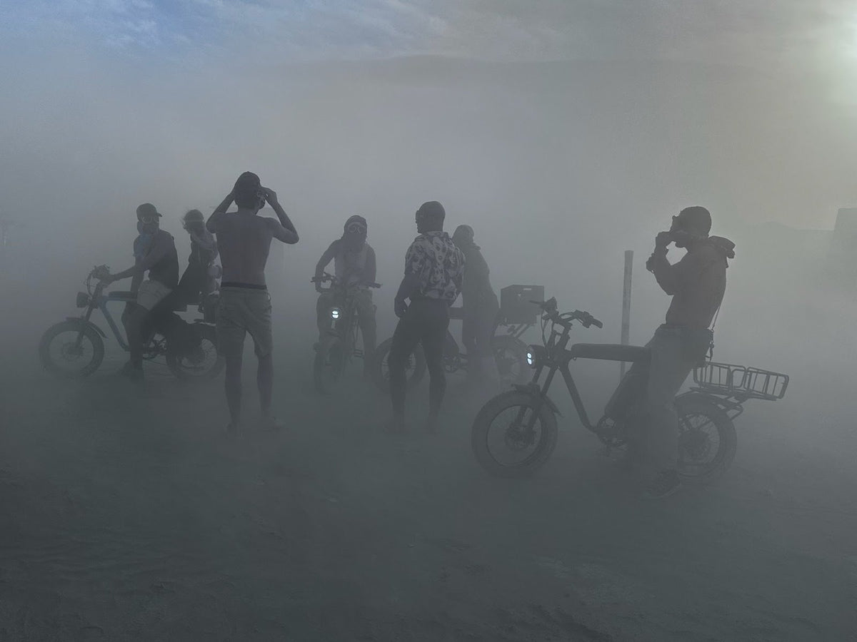 Cyclists and bikes silhouetted in a thick dust storm at a desert festival camp